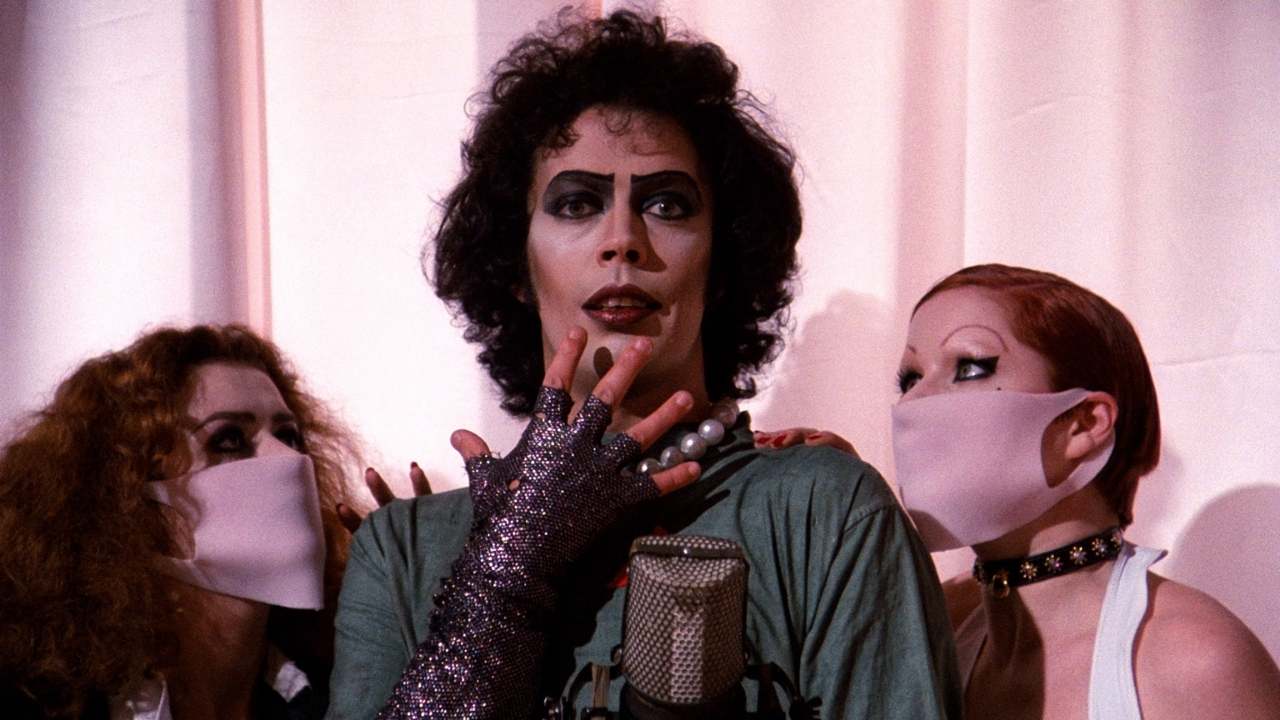 Tim Curry in drag next to two women in masks